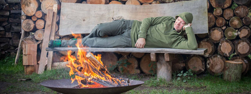 Mand hviler på bænk ved udendørsbål